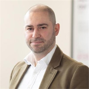 Matthew Heyworth in a brown jacket and white shirt, in front of a pale background