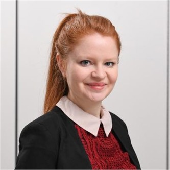 Victoria Potts wearing a red top, black blazer in front of a grey background.