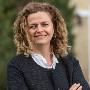Melissa Lesson in a black jacket and yellow top, in front of a grey background