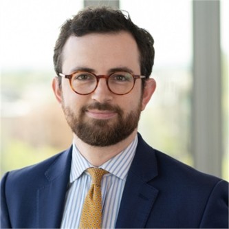 James Prothero in glasses, a blue jacket and yellow tie, in front of a window