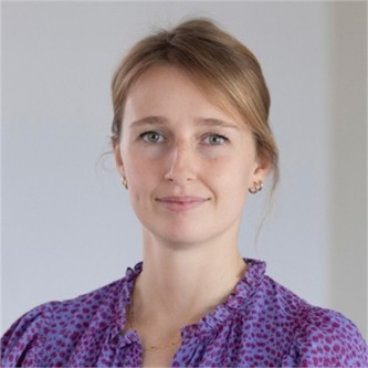 Annie Wogel in a purple patterned top, in front of a grey background