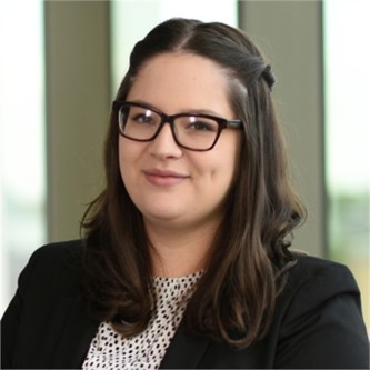 Sophie Martin in glasses, a black jacket and white spotted top, in front of a window
