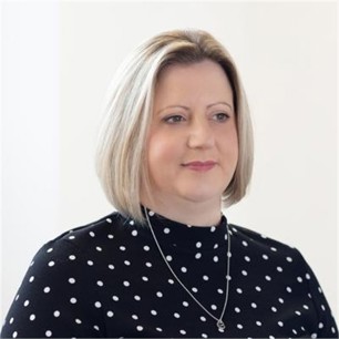 Claire Burton in a black polka dot top, in front of a grey background