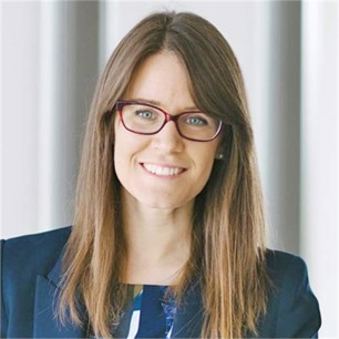 Ania Tarasiewicz in a navy jacket and glasses, in front of a grey background
